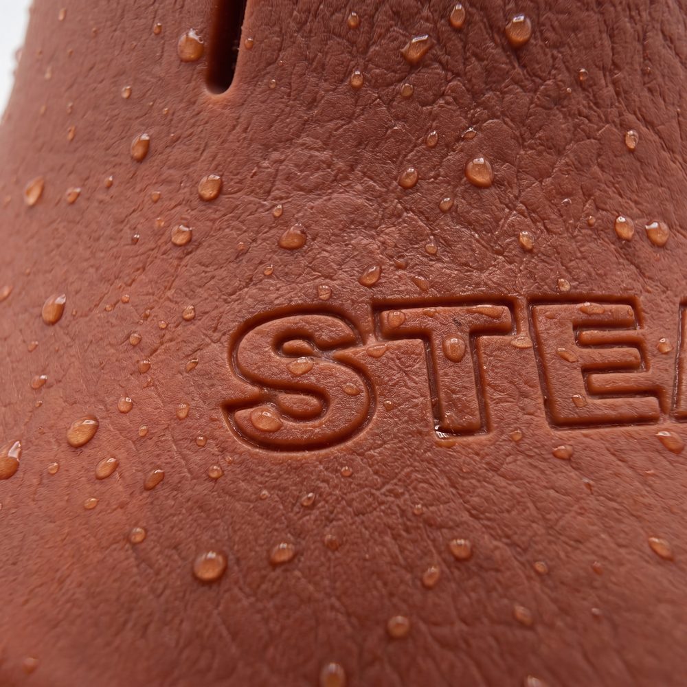 Water beading on the matte terracotta surface of a Steadi, across the moulded STEADI mark.