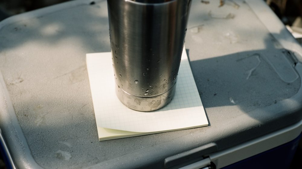 A tumbler standing on a yellow sticky note on a cooler lid.