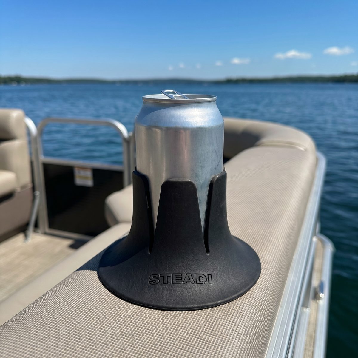 A can standing in a black Steadi on a boat bench cushion, water behind it.